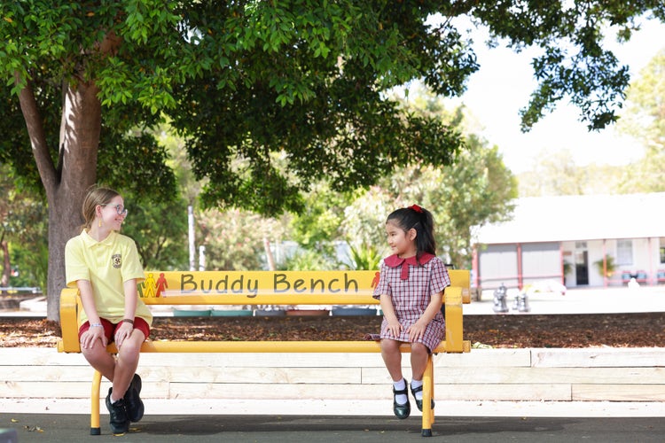 Two stidents smiling at eachother on a buddy bench